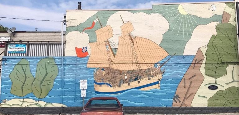 A mural painted on a wall depicts a large boat sailing across the water to shore under green-painted sunny skies.
