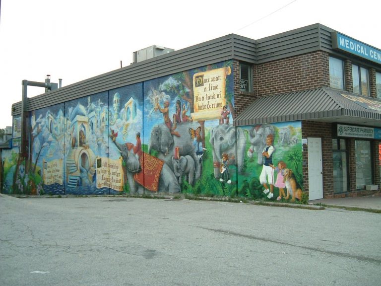 A mural, painted on a wall, depicting a fantasy world featuring elephants and riders, alongside spired, cloud-topped towns appear among the words "Once upon a time in a land of hate and crime..." written on a scroll.