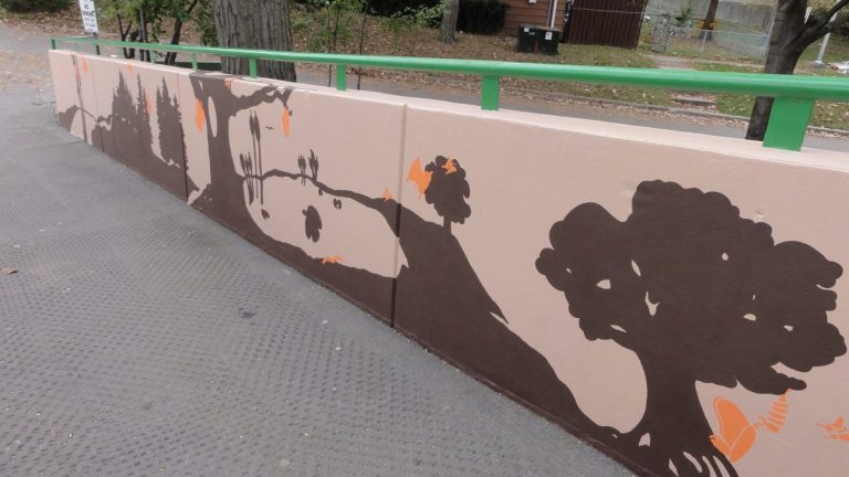 A mural of tree's silhouettes, lake outlines, trees and paths are painted in brown on a pink background. Orange butterflies fly in between.