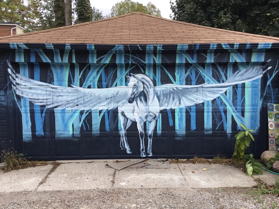 A mural of a white Pegasus in a light blue forest, painted on a garage.
