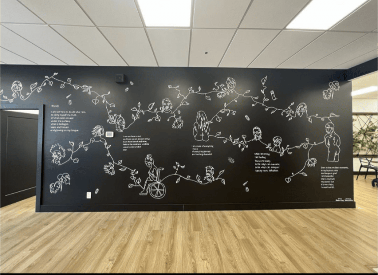 A mural of white white painted vines that curve into outlines of eleven humans on a black wall. Between gaps in the vines are verses of poetry.