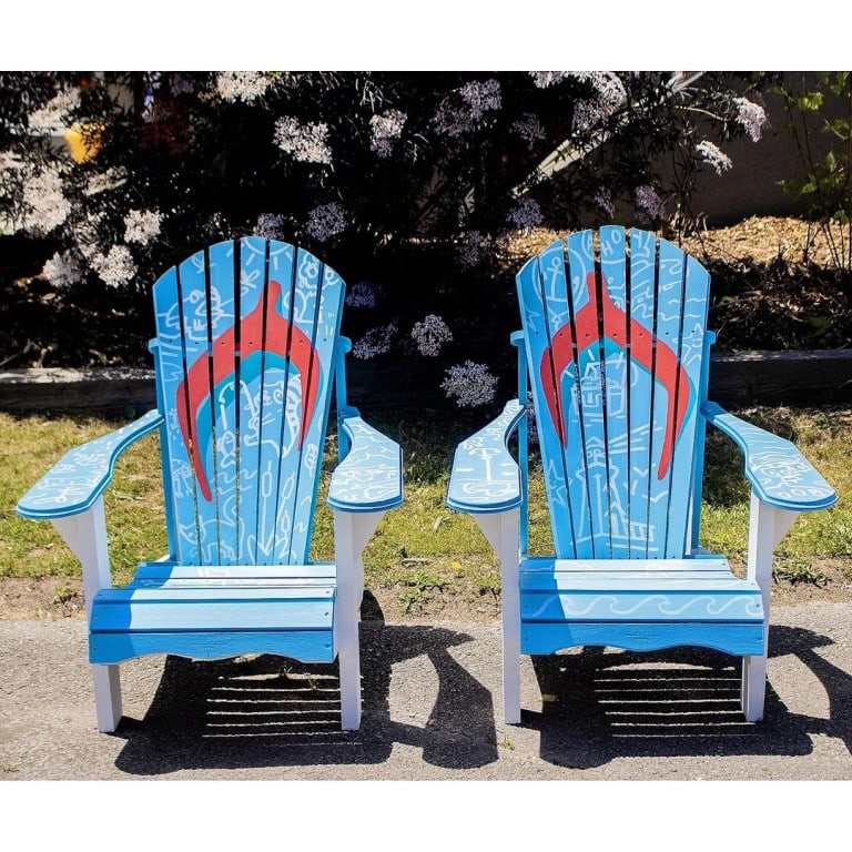 Two light blue Muskoka chairs, painted with red wishbone-like shape in the middle, to give the illusion of flip-flops. White details of lighthouses, treasure, raccoons fishing, reeds, and anchors create a busy and dynamic background.