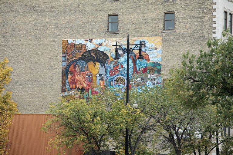 A scene of several women seen from different angles, poses, and performing different tasks. Certain elements of the work are created in an illusionist fashion, as hidden images of women can be noticed throughout. Behind the women are elements of nature such as bodies of water, green mountains, a sky with clouds, and animal bones seen to the right.