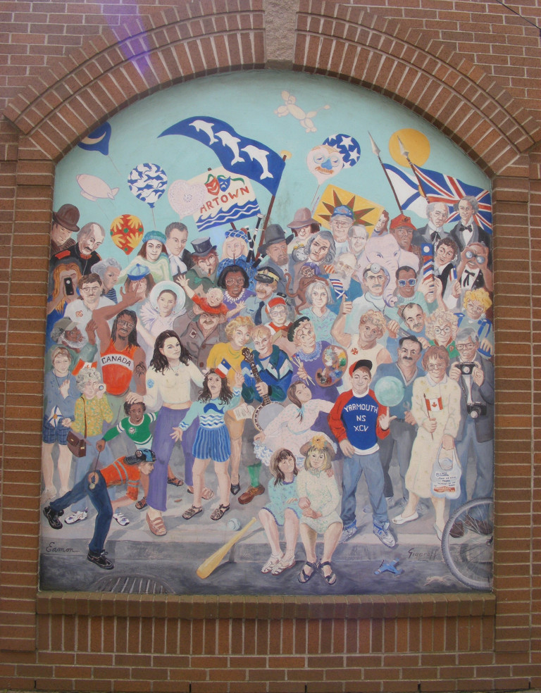 A crowd of people are gathered in this mural. They're standing on the sidewalk in a celebratory mood while some children sit on the curb in the foreground. Some wave Nova Scotian flags, some wave British flags. Some of the figures are historical, while others are more contemporary.