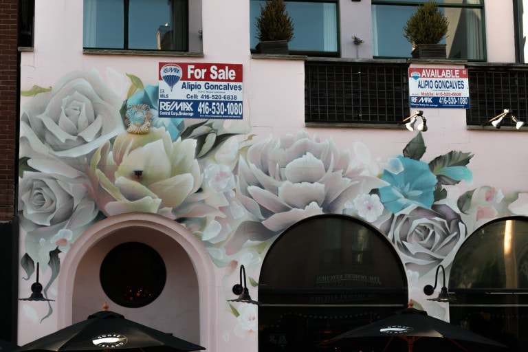 Image of the archways of a building complex focusing on the mural painted by Vizsla Bacon. Background is white and his signature wispy florals adorn the top in pastel pinks, yellows and blues.