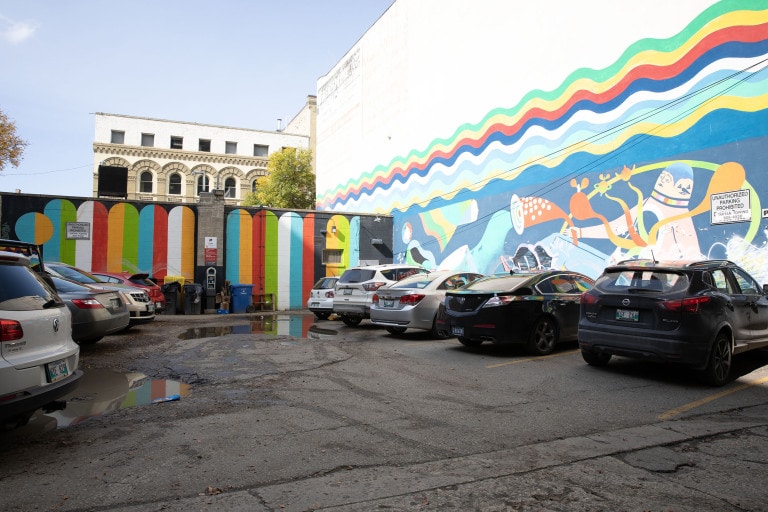 On a black background, thick, bright lines are arranged side by side horizontally, and rounded at the top. The solid coloured stripes are an alternating red, green, white, orange, blue and black. On the right hand side is a circle; blue on one side and orange on the other.