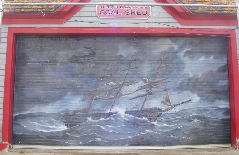 Bordered by a red frame, a ship with three masts is battling tall waves. Dark clouds loom overhead, but there appears to be bits of blue sky poking through the storm. The colour palette is various shades of grey.