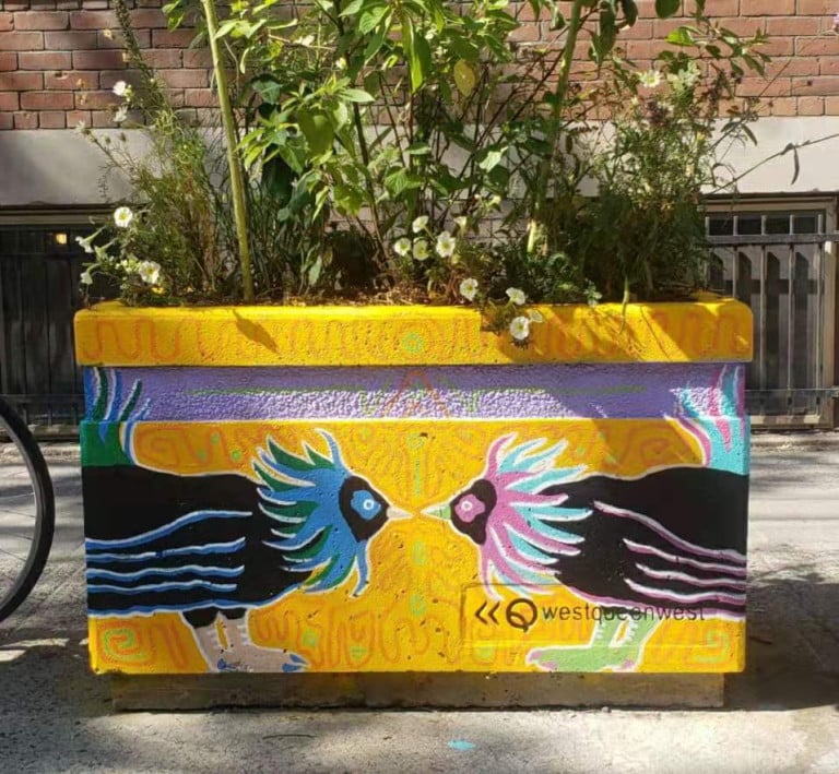 A planter mural of a pair of fighting roosters facing each other at the same level with a yellow background of patterned motifs.