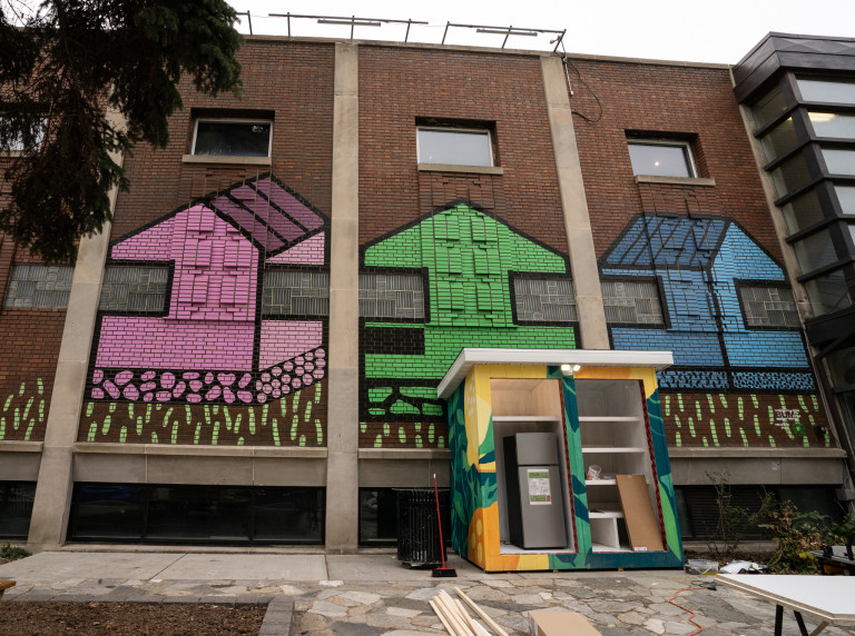 From left to right. Purple/pink house with grass below, green house in center and blue house at right end.