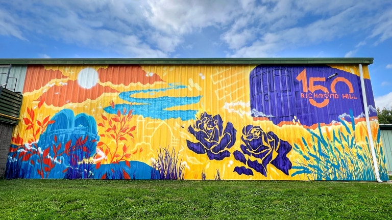 A large mural with golden-yellow, dark purple, burnt orange and teal, features depictions of a radial train, iconic landmarks like the Richmond Hill David Dunlap Observatory, and elements of the City’s natural environment. It also includes roses commemorating Richmond Hill once being dubbed the “Rose Capital of Canada”, and wheat sheaths symbolizing the City’s humble beginnings as a farming town.