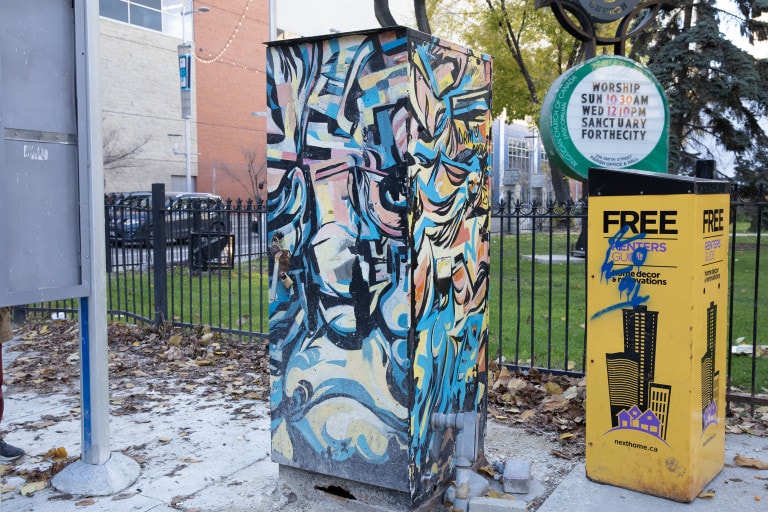 A transit box depicting an abstract scene of lines and shapes, with varying colours of blue, yellow, orange and pink, outlined in black.