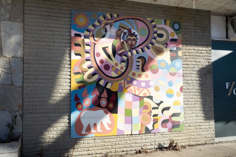 Abstract painting with many colours, patterns and shapes. Two figures seen in the top centre. There is also a silhouette of a bear in the bottom left corner.