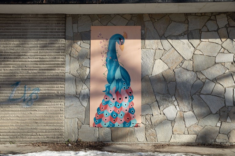 Blue, red and pink peacock is painted on an orange background. Small flowers wrap lightly around the bird's neck.
