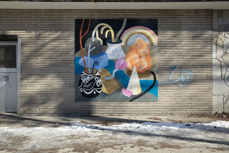 Brightly coloured lamps and vases are set up between a passing river. The pots contain vines and flowers. On a black background, a rainbow is seen in the distance.