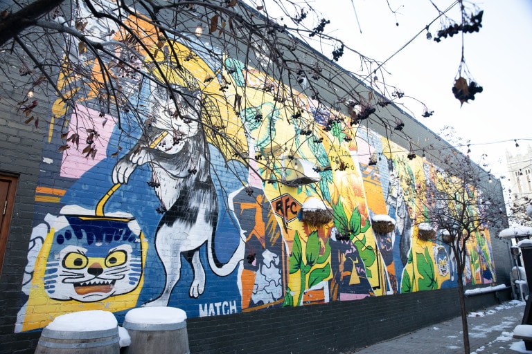 Mural with repeating images, separated by painted rips. Images of birds, cats, plants, and various abstract patterns.