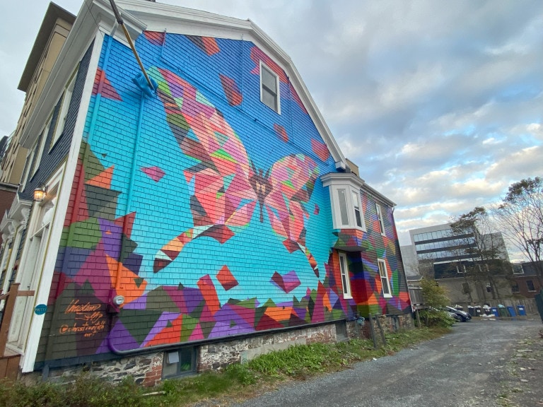 The entirety of the side of a building is painted with a geometric butterfly. The butterfly is comprised of multi-coloured triangles and trapezoids.