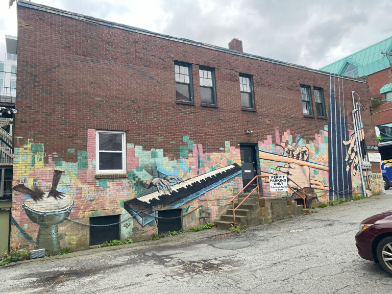 The entirety of a wall is painted in muted, peachy tones, depicting various instruments. Hands play a keyboard, a hand drum, a trombone and the neck of an upright bass.