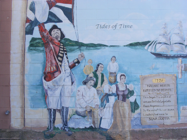 A group of people in historical, Loyalist-era clothing stand in front of the ocean, ships and islands in the background. A man in the foreground waves a Union Jack and a scroll reads: "1776 YOU ARE HEARBY NOTIFIED TO DEPART"