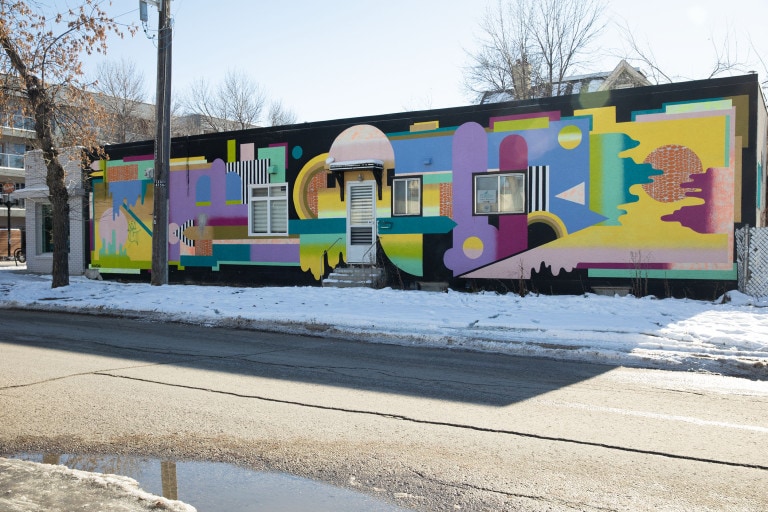 An array of different shapes, colours, patterns and gradients incorporated onto a black wall. These shapes go in all various directions and compliment the infrastructure of the building.