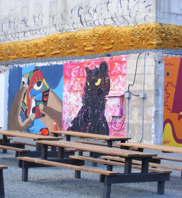 A black cat is painted with squiggles on the side of a wall. The cat has bright yellow eyes and is set against a pink background.