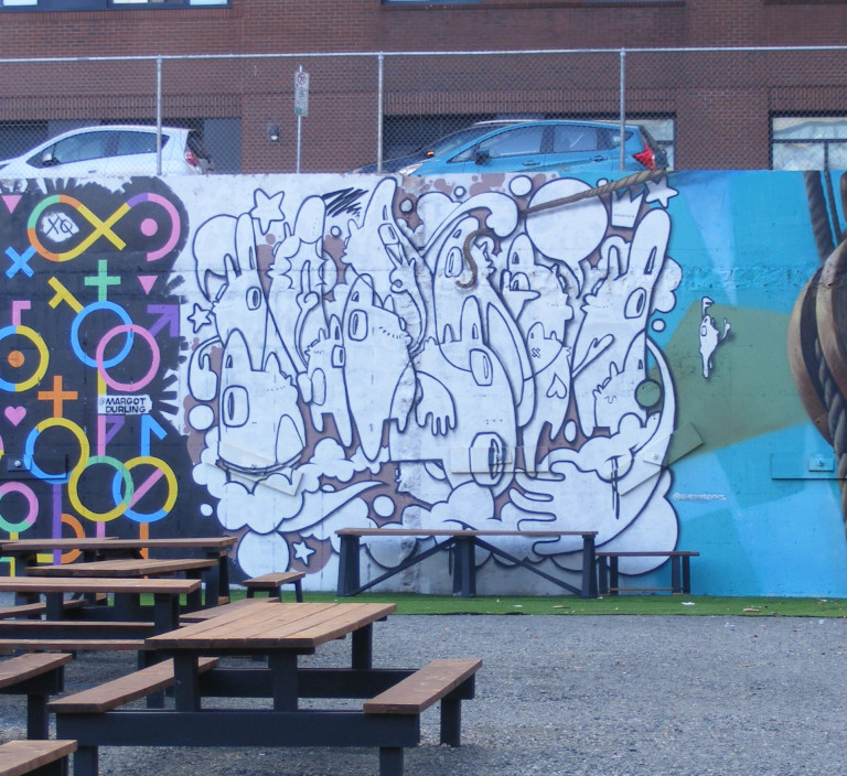 Black and white cartoon characters are painted on the side of a wall, flanked by two murals on the right and left.