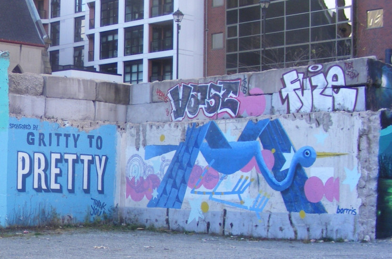 The wall is painted with a geometric blue crane in front of pink circles and swirls. The "Gritty to Pretty" logo is painted on the wall to the left.