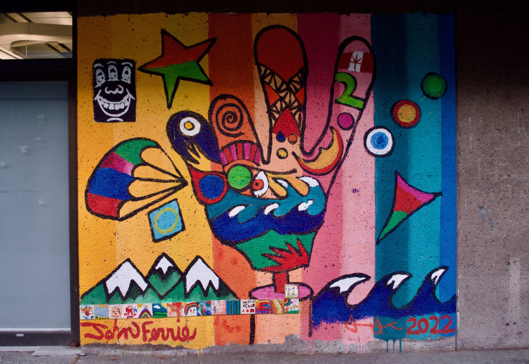 A colourful abstract mural on the side of a community centre depicts the sea, mountains, and other unique figures