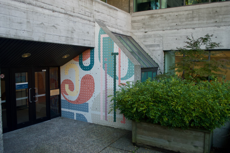 A colourful, uniquely shaped mural on a brutalist style building.