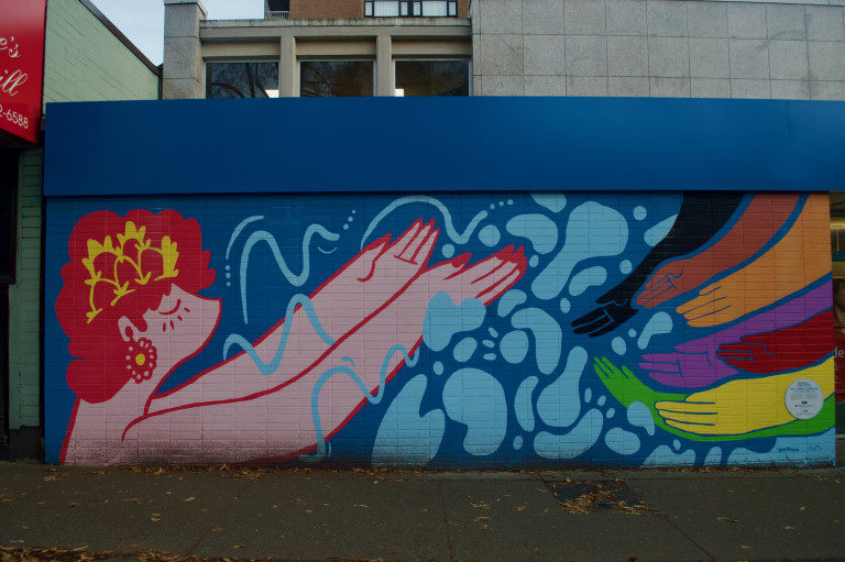 A pink figure extends their hands to several arms in the progress pride colours