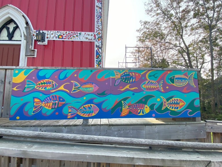 A board decorated with multi-coloured fish set against blue, purple and green waves are displayed on the railing of a wooden ramp.