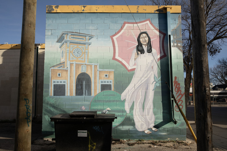 Three Vietnamese women stand in front of buildings and scenery of different regions of Vietnam. One woman holds an umbrella, another holds a basket of flowers. The last woman holds a Classic Conical Coolie hat.