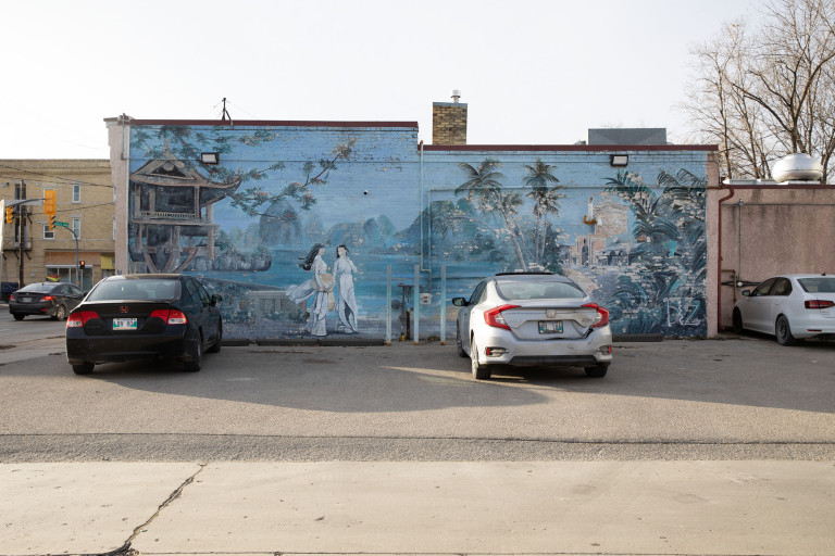 Two women are seen walking on a beach in Vietnam, with a view of the mountains, trees and architecture of the country.