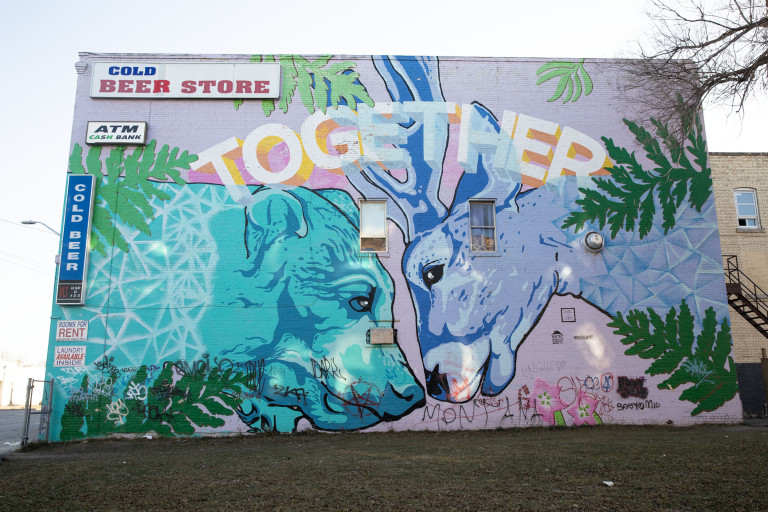 On a pale purple background, a teal bear and a blue deer stand facing eachother with their noses touching. A few leafs apear from the edge of the painting, and the word the 'together' displayed at the top.