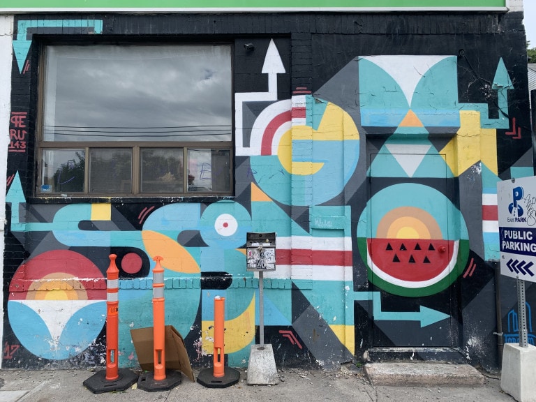 Photo of a mural over a door and around a window with a black background. Abstract shapes in a predominately blue tone decorate the mural, with one circular shape having a watermelon as the other half.