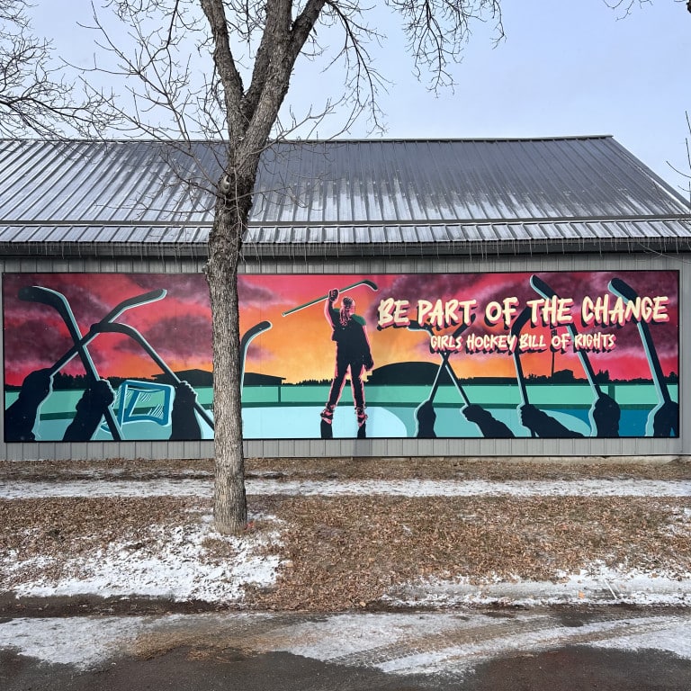 Colourful mural painting for a sunrise, girl hockey player holding up a hockey stick, other hands holding up hockey sticks, town silhouette, hockey rink, and text “Be Part of the Change Girls Hockey Bill of Rights”