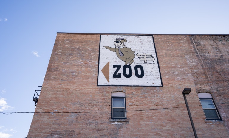Yogi bear framed in a black border, "ZOO" test arrow on left side. Sign on right side with arrow pointing to the left reads, "ST GEORGES ISLAND" and "JELLYSTONE PARK" arrow point to the right