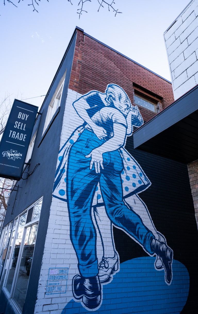 Woman figure kissing male figure. Woman holding man by waist. Woman in polka dot skirt. In shades of blue and white.