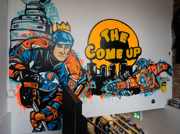 Edmonton Oilers hockey player in skating mode with Stanley cup in background. Another hockey player on right side with city silhouette skyline in background.