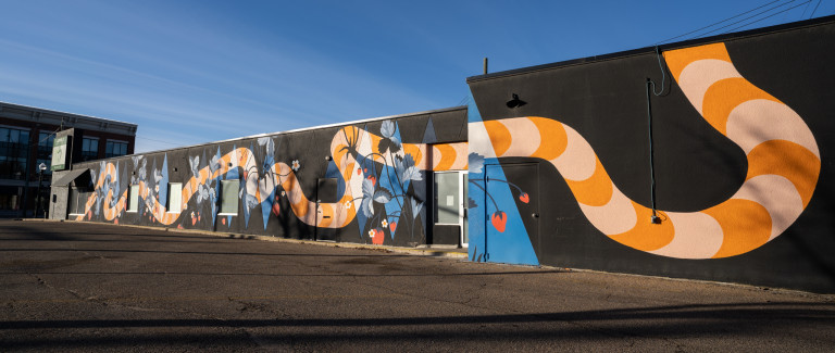 Orange and peach patterned snake figure horizontally spread through entire walls of building with strawberries, small daisies and blue leaves on top and behind snake.