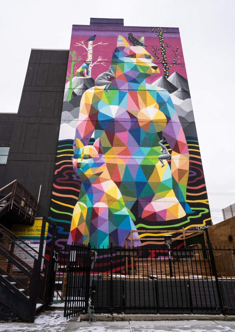 Geometric fox/wolf hybrid with human and colourful geometric cat on left side. Hanging nude women bodies around fox/wolf hybrid. Water like lines in rainbow colours surround bottom of figures.