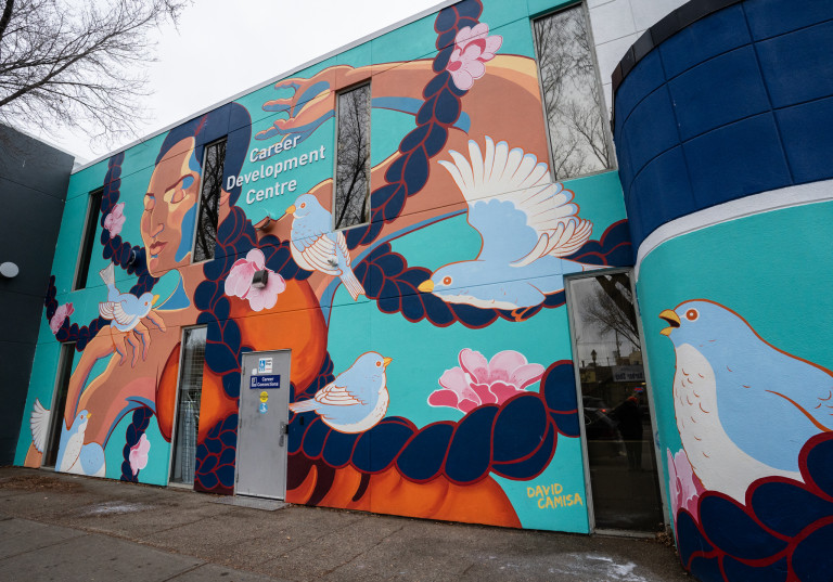Woman figure with braided hair and orange/brown dress expanding throughout walls. Light blue birds spread out over the lady.