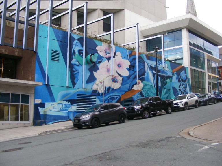 This photo is a wide shot. The side of a building is painted in various shades of blue. A woman's face can be seen staring forward.