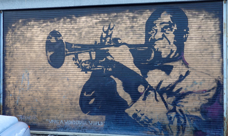 A portrait in gold and black of Louis Armstrong playing the trumpet and the words "What a Wonderful World"