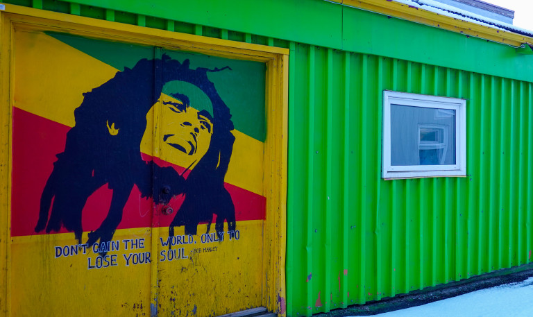 Portrait of Bob Marley in front of a Rasta flag on a door of the South side of the Pickapeppa Caribbean Soul Food restaurant. Under the portrait it has the Bob Marley quote "Don't gain the world only to lose your soul".