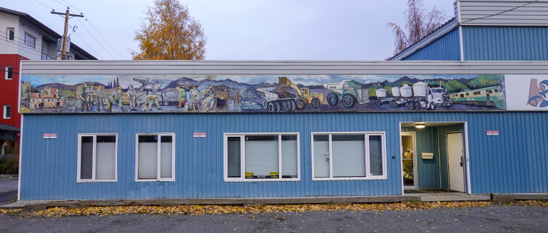 Long horizontal mural along the top of the Chamber of Mines building showing the history of mining in the Yukon.