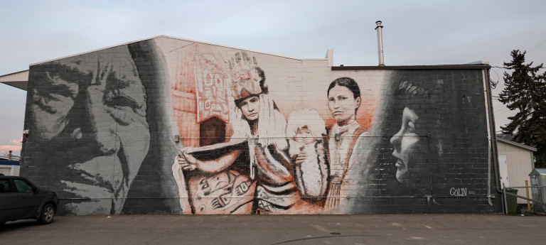 Mural depicts a First Nation family and two shadowed faces of a child and an elder.