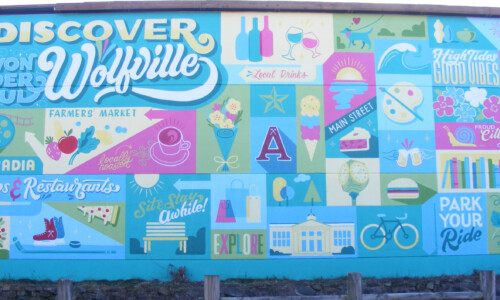 "Discover Wonderful Wolfville" is written in the top left corner. The rest of the mural is a patchwork of symbols that represent Wolfville: skates, fresh produce, bikes, apples, Acadia University, coffee cups, wine bottles and more.