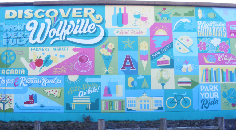 "Discover Wonderful Wolfville" is written in the top left corner. The rest of the mural is a patchwork of symbols that represent Wolfville: skates, fresh produce, bikes, apples, Acadia University, coffee cups, wine bottles and more.