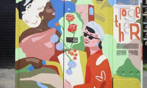 Photo of a bell box mural featuring a range of smiling people of different genders and ethnicities, painted in colourful block colours. On the right, it’s written “Together” in a whimsical style.